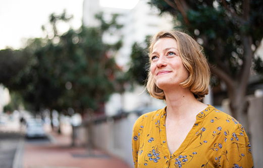 Young woman looking up and smiling while standing alone outside on a sidewalk in the city