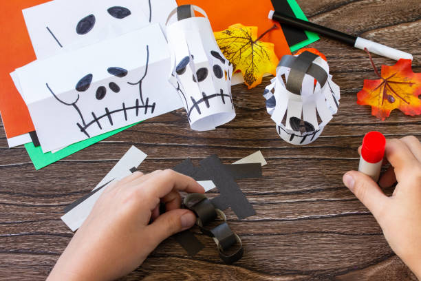 istock Instruction step 7. Child creates Halloween decor, paper lanterns garland skull for Halloween. Childrens art project, crafts, fun activities for kids. 1279946745