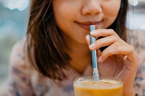 Young asian woman drink coffee using metal straw. Reducing paper or plastic waste.
