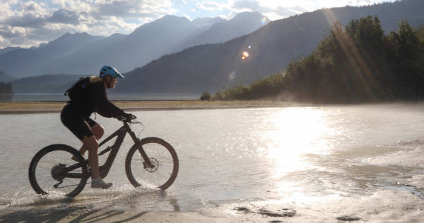 istock Female mountain e-biker rides along lakeshore at sunrise 1279952370