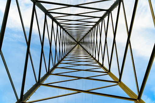 Upwards view insided an electricity pylon with blue sky and clouds in the background.