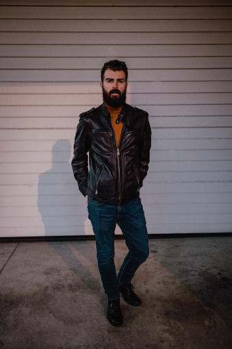 Portrait of a handsome bearded man wearing a leather jacket in the city street on an autumn day