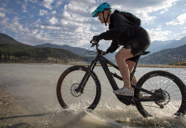 Female mountain e-biker rides along lakeshore at sunrise