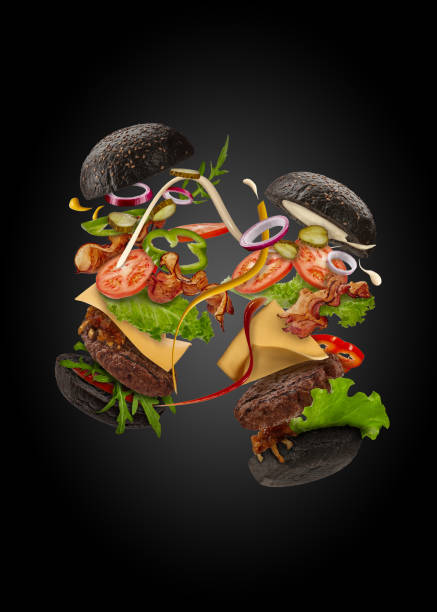 istock Two palatable black burgers with flying ingredients on black background. Ham, beef cutlet, cheese, sauces, vegetables and greens. Close up, copy space 1279953472