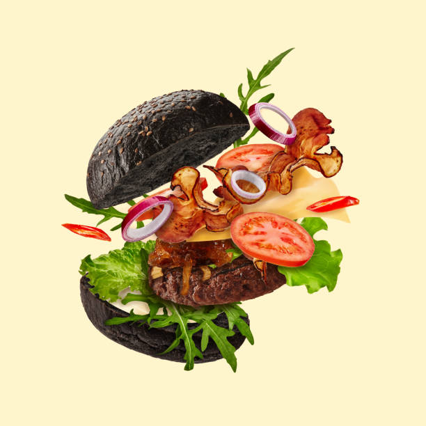 istock Fresh black burger with flying ingredients on beige background. Ham, beef cutlet, cheese, sauces, vegetables and greens. Close up, copy space 1279953502