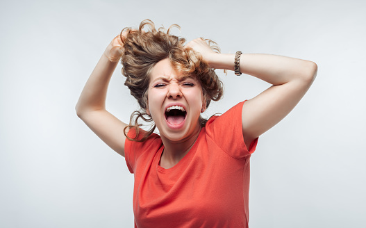 Image of stressed blonde girl with curly hair in casual t shirt grabbing her head. Emotional helplessness. Problems, surprise, fear, fobia concept. Studio shot, white background.