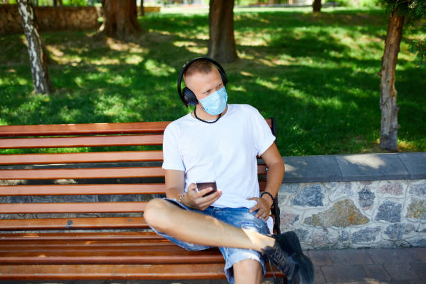 istock Man listening music with headphone, using smartphone wearing protective mask outdoor 1279955821
