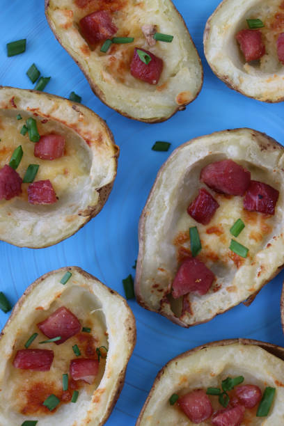 Full frame close-up image of group of baked potato skins loaded with melted cheese, bacon cubes and sour cream, garnished with a sprinkling of chopped chives, served on turquoise blue plate, elevated view