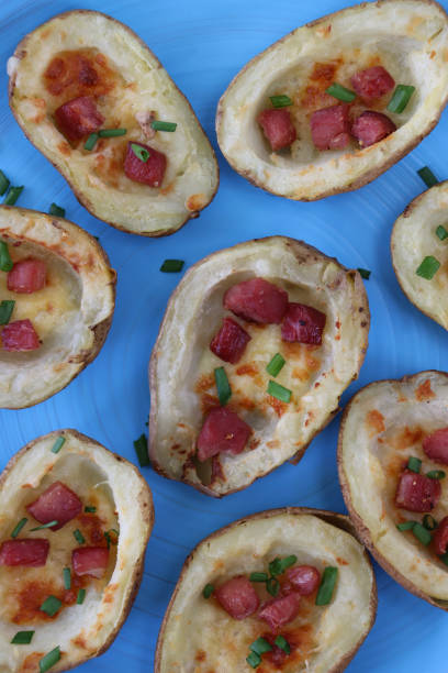 Full frame close-up image of group of baked potato skins loaded with melted cheese, bacon cubes and sour cream, garnished with a sprinkling of chopped chives, served on turquoise blue plate, elevated view