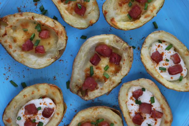 Full frame close-up image of group of baked potato skins loaded with melted cheese, bacon cubes and sour cream, garnished with a sprinkling of chopped chives, served on turquoise blue plate, elevated view
