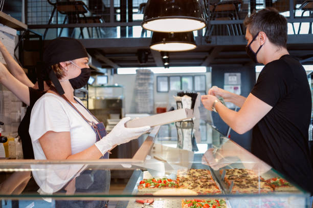 istock Checkout server about to give pizza box to customer who is using alcohol to clean and wash hands 1279959845
