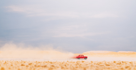 A small red car races across the desert. Model photography.