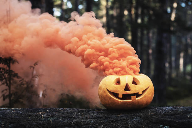 istock carved halloween pumpkin with orange smoke on tree trunk in forest 1279961155