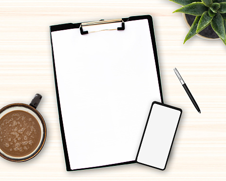 A paper holder pad with white sheets attached, Workspace Mockup, Paper sheets, cup of coffee, cell phone, pen and green plant on office desk, copy space