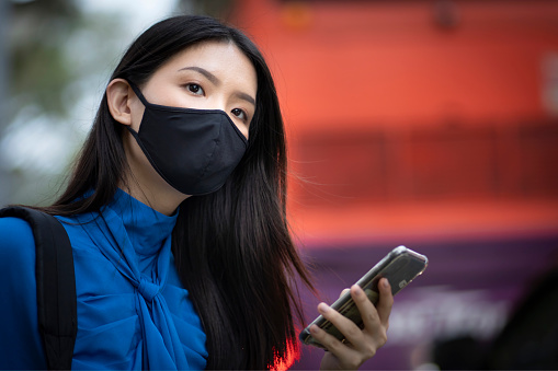 Asiática joven mujer adulta que lleva máscara de la cara mirando hacia fuera para taxi reservado photo