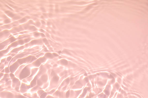 pink transparent clear water surface texture summer background de-focused. Closeup of pink transparent clear calm water surface texture with splashes and bubbles. Trendy abstract summer nature background. Coral colored waves in sunlight. coral colored photos stock pictures, royalty-free photos & images