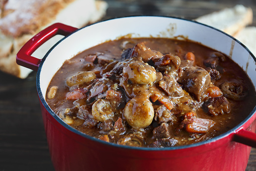 Beef Bourguignon or Boeuf cooked in an enameled cast iron Dutch oven and served with homemade artisan bread over a rustic wood background.