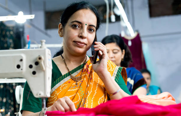 istock Indian woman textile worker talking on mobile phone while sewing dress fabric 1279972521