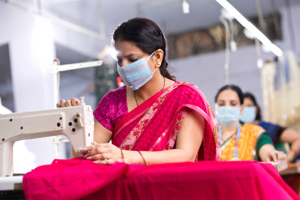 Indian woman textile workers with protective face mask on production line Indian woman textile workers sewing clothes with protective face mask on production line woman stitching stock pictures, royalty-free photos & images