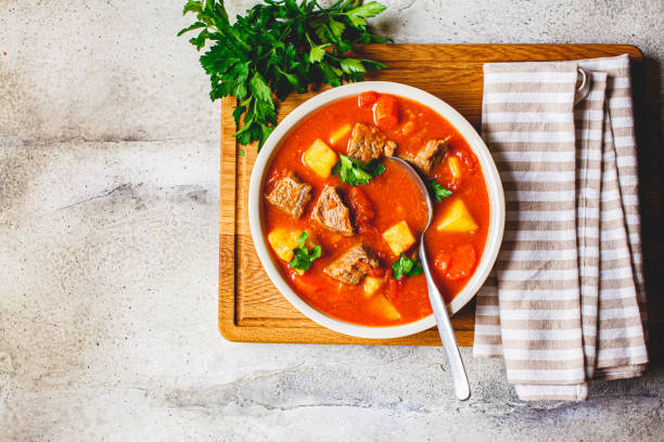 Soup with beef and vegetables in white plate on a wooden board, copy space, top view. Traditional meat shurpa soup with vegetables and herbs.