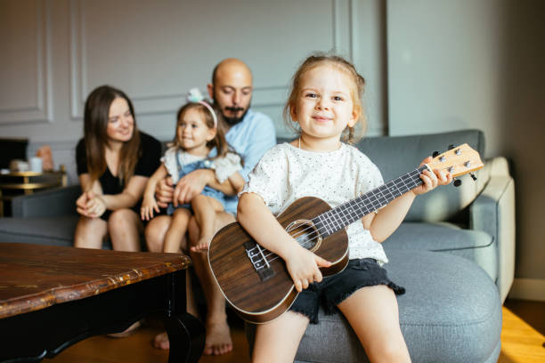 istock Happy little girl is smiling while playing a ukulele during a private music learning lesson at home 1279981194