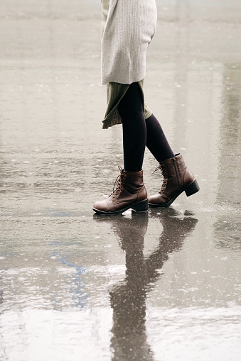 Closeup of woman's legs walking on wet asphalt in rainy day