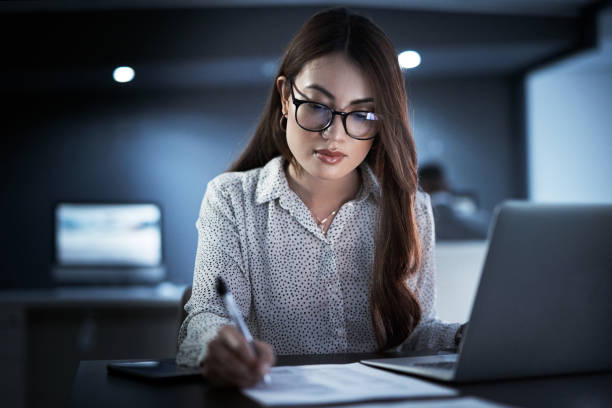 She won't leave until her paperwork is all in order Shot of a young businesswoman going through paperwork while working in an office at night cash flow photos stock pictures, royalty-free photos & images