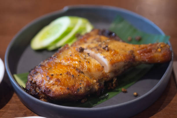 istock Grilled herb chicken style Thai ancient, chopped served with slice cucumber in black dish on wood table. Select focus 1279984385