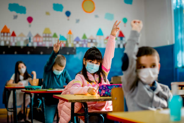 Elementary schoolchildren wearing a protective face masks in the classroom. Education during epidemic. Elementary schoolchildren wearing a protective face masks in the classroom. Education during epidemic. social distancing photos stock pictures, royalty-free photos & images