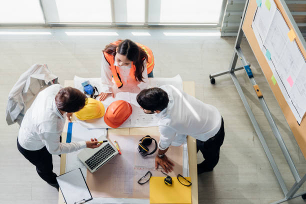 vista superior do engenheiro jovem asiático e caucasiano usar capacete de segurança em nova reunião de projeto. trabalho em equipe engenheiro consultor consultor empreendedor casual brainstorm. indústria, engenheiro e conceito de construção. - safety meeting construction site construction - fotografias e filmes do acervo