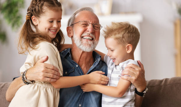 großvater umarmt enkelkinder auf sofa - family smiling adult love stock-fotos und bilder