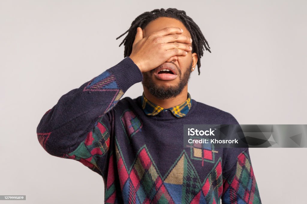 Angry shocked african guy with beard and dreadlocks closing eyes with hand, hiding, dont want to see and know, ignorance Angry shocked african guy with beard and dreadlocks closing eyes with hand, hiding, dont want to see and know, ignorance. Indoor studio shot isolated on gray background Shame - Negative Emotion Stock Photo