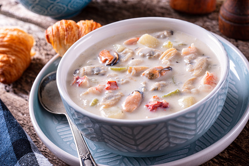 A bowl of delicious seafood chowder with fresh clams, mussels, lobster, shrimp, scallops, potato, celery and cream.