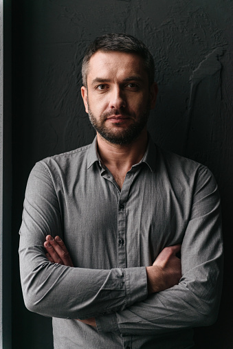 Image of handsome man standing over dark background looking at camera.