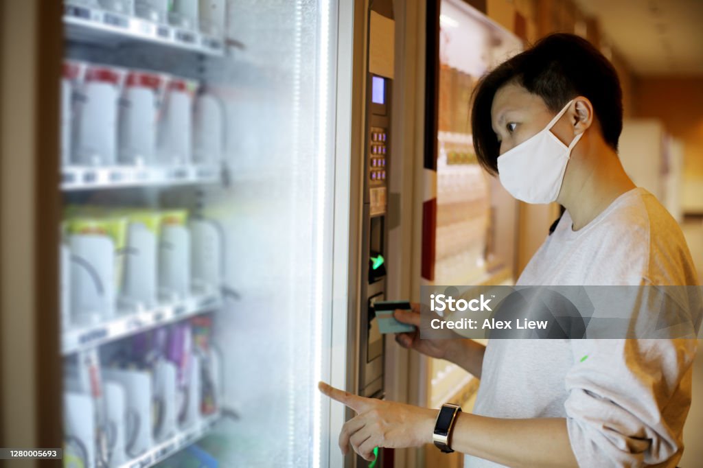 The New Norm A Chinese female adult is using credit card for contactless payment at vending machine. She is seen wearing face mask as part of the new norm in Malaysia. Vending Machine Stock Photo
