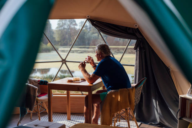 Enjoying the Peace and Quiet Man sitting in a dome tent at a glamping site in Northumberland. He is sitting at a table beside a window having a drink. glamping photos stock pictures, royalty-free photos & images
