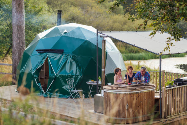 Glamping in Alnwick Wide shot of a family sitting together around hot tub with a lid that is being used as a table on a patio eating and drinking at a lakeside glamping site in Northumberland. glamping photos stock pictures, royalty-free photos & images