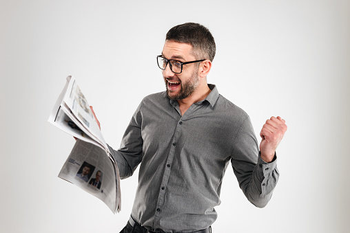 Image of happy businessman standing isolated over white background reading newspaper.