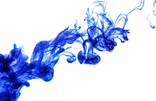 Blue ink injected into water from syringe, colour mixing with water creating abstract shapes, white background