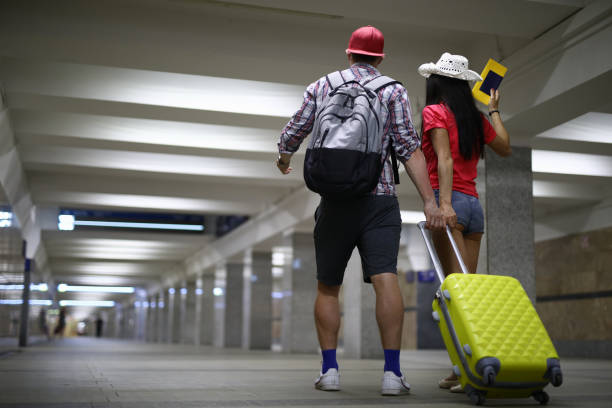 istock Couple stand with their backs and hold yellow suitcase by handle in underground passage. 1280009959
