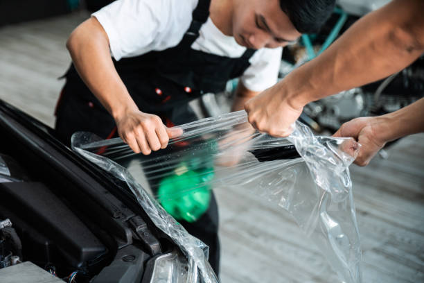 istock PPF installation process, close-up stretching removing an old transparent film on a car headlight and hood by hand. Automobile professional service. 1280011138