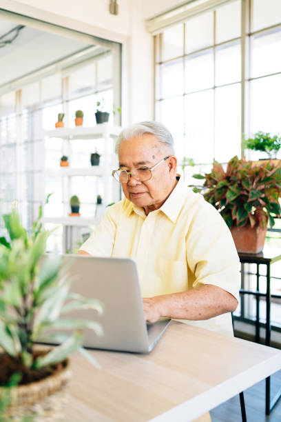 istock A senior retired old man dressed in casual style is using a laptop and smiling while sitting at home with indoor garden in the background. Retirement hobby and lifestyle. Grandfather work from home. 1280011161