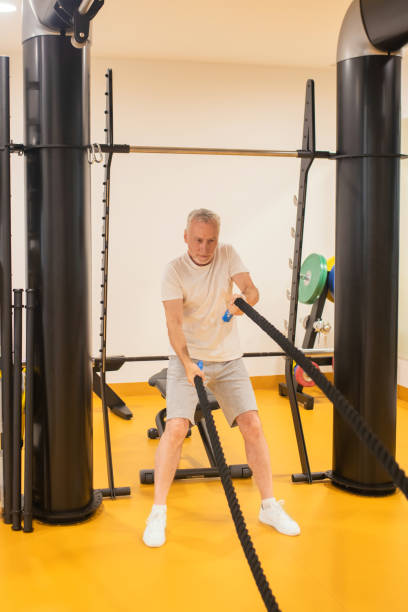 istock Grey-haired man in sportswear pulling the ropes in gym 1280012308