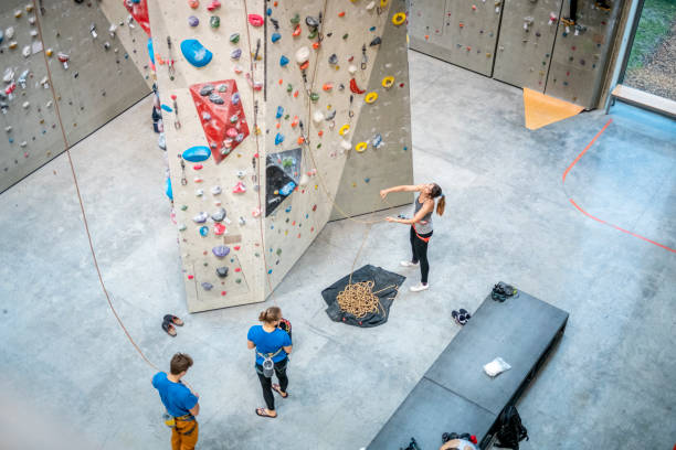 Belayers Standing on Floor of Modern Sport Climbing Gym High angle view of young male and female belayers working in tandem with climbing partners scaling vertical pillar in indoor facility. high resolution stock pictures, royalty-free photos & images