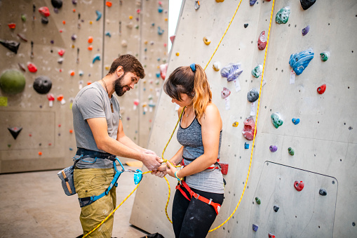 Side view of male and female climbing partners in their 20s preparing equipment for workout in modern indoor gym.