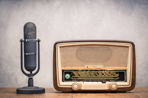 istock Retro broadcast table radio receiver with green eye light, studio microphone circa 1950 on wooden desk front concrete wall background. Listen music concept. Vintage old style filtered photo 1280018195
