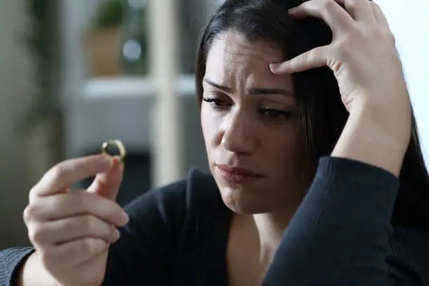 Sad doubtful wife looks at wedding ring thinking in divorce
