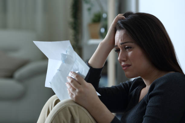 sad woman reading a letter alone at home - declaring bankrupcy imagens e fotografias de stock