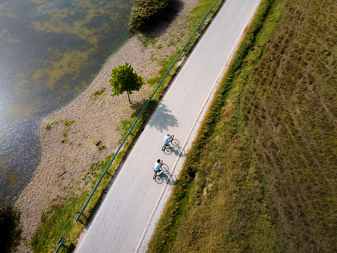 Two men riding bicycle by the lake outdoors to stay fit and healthy aerial top view. Cycling, sports and quality family time in the nature abstract