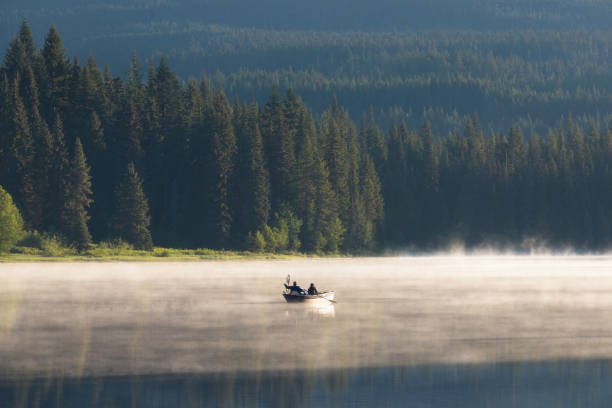 homme sur un canot. les montagnes se reflètent sur les eaux calmes du lac sparks au lever du soleil dans la chaîne cascades dans le centre de l’oregon, etats-unis dans une lumière tôt le matin. la brume matinale s’élève du lac dans les arbres. - sea zen like landscape water photos et images de collection